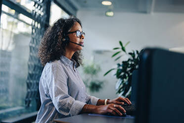 Geschäftsfrau, die am Computer arbeitet und über ein Headset spricht. Berufstätige Frau mit Headset, die an ihrem Schreibtisch arbeitet. - JLPSF05279