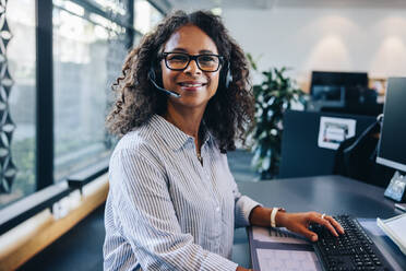 Porträt einer selbstbewussten weiblichen Führungskraft mit Headset, die im Büro sitzt. Geschäftsfrau mit Headset, die in die Kamera schaut und lächelt. - JLPSF05282