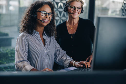 Zwei Geschäftsfrauen, die lächelnd auf einen Computerbildschirm schauen. Reife Geschäftsleute, die in einem Callcenter zusammenarbeiten. - JLPSF05288