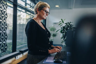 Senior businesswoman working in office. Mature female professional working at standing desk in modern office. - JLPSF05293