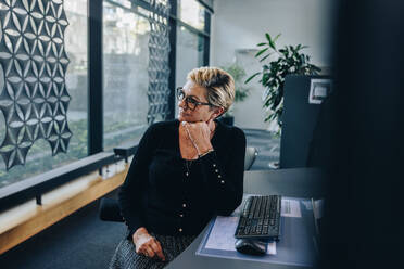 Corporate professional sitting at her desk looking away with hand on chin. Stressed businesswoman relaxing at her desk. - JLPSF05298