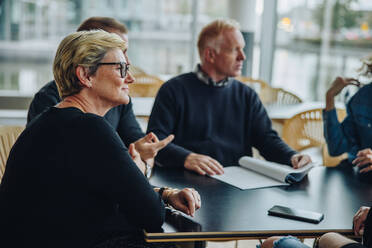 Eine ältere Geschäftsfrau sitzt in einer Besprechung im Sitzungssaal. Eine Gruppe von Geschäftsleuten hat eine Besprechung im Büro. - JLPSF05314