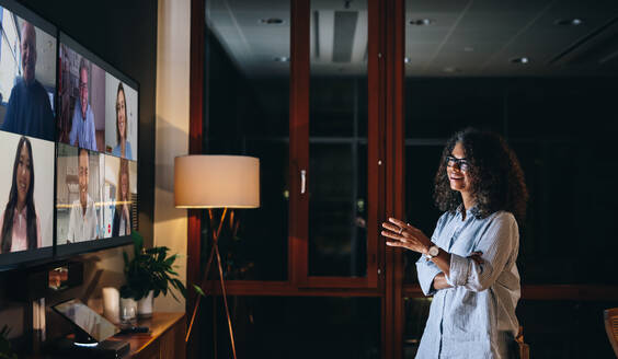 Businesswoman talking to teammates over a late night video call. Entrepreneur talking with coworkers on lcd tv. - JLPSF05376