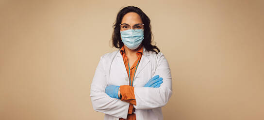 Portrait of a female doctor wearing protective face mask and gloves. Healthcare worker standing with her arms crossed. - JLPSF05439