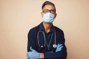 Portrait of a male doctor wearing protective face mask and gloves. Healthcare worker standing with his arms crossed. - JLPSF05484