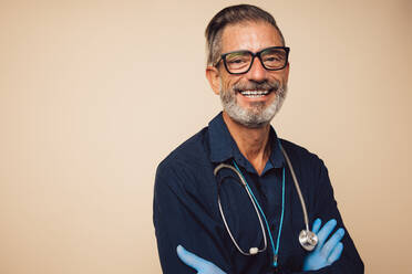 Portrait of a confident doctor with stethoscope wearing protective hand gloves. Physician looking at camera and smiling with his arms crossed. - JLPSF05486