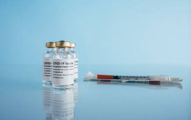 Corona-Virus-Immunimpfstoff-Fläschchen und Spritze auf blauem Hintergrund. Covid-19-Impfflaschen mit Injektion auf reflektierender Oberfläche. - JLPSF05513