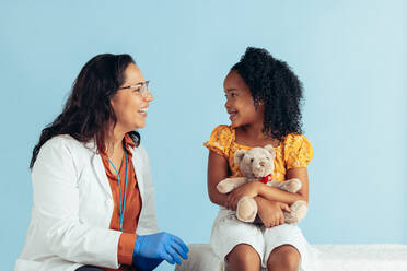 Doctor and girl smiling on blue background. Smiling pediatrician talking with cute patient in clinic. - JLPSF05532