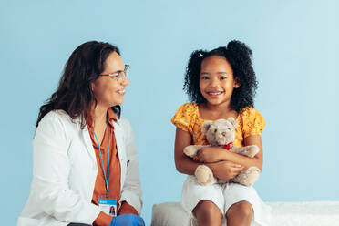 Arzt und Mädchen Patientin Mädchen in der Klinik. Lächelnde Kinderärztin mit niedlichen Patienten auf blauem Hintergrund. - JLPSF05533
