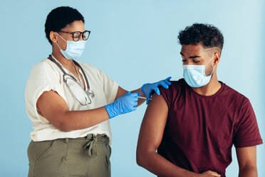 Female doctor wearing face mask and gloves giving vaccine to a man against blue background. Man getting vaccinated by a female doctor. - JLPSF05538