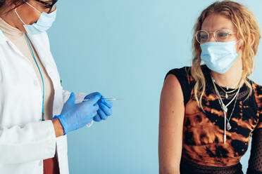 Junge Frau mit Gesichtsmaske in der Klinik, die den Impfstoff Covid-19 erhält. Arzt bereitet Impfstoffinjektion für Immunisierung vor. - JLPSF05553