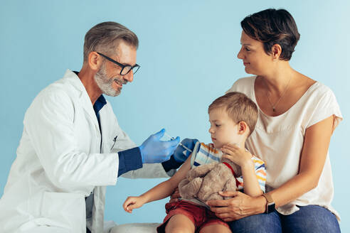 Arzt gibt einem kleinen Jungen, der mit seiner Mutter in der Klinik sitzt, eine Grippeimpfung. Ein Junge wird von einem Kinderarzt geimpft. - JLPSF05567