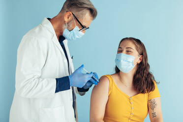 Woman wearing face mask closing her eyes while getting vaccine on her arm. Male doctor giving vaccination to a woman. - JLPSF05574