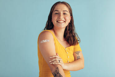 Porträt einer jungen Frau, die ihren Arm zeigt, nachdem sie eine Impfdosis erhalten hat. Frau mit Verband am Arm nach der Impfung auf blauem Hintergrund. - JLPSF05580