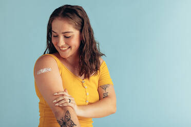 Frau betrachtet ihren Arm mit Pflaster, nachdem sie eine Impfdosis erhalten hat. Frau wird geimpft. - JLPSF05581