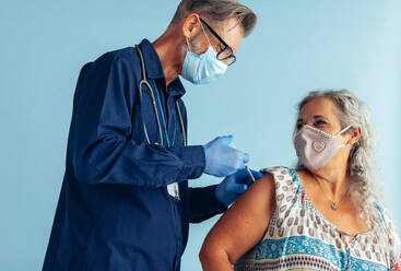 Senior woman getting second coronavirus vaccine dose for full immunity. Doctor giving vaccine to senior female wearing face mask during pandemic. - JLPSF05584