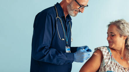 Doctor putting band-aid on arm of a senior woman after giving vaccine. Senior female getting vaccinated by a medical professional. - JLPSF05587