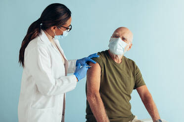 Female doctor giving coronavirus vaccine to senior man. Medical professional and elderly man wearing protective face masks during coronavirus immunity vaccination. - JLPSF05599