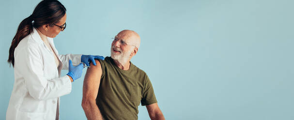 Ein älterer Mann erhält eine Impfdosis von einem Arzt. Ein Arzt gibt einem älteren Mann auf blauem Hintergrund einen Impfstoff. - JLPSF05601