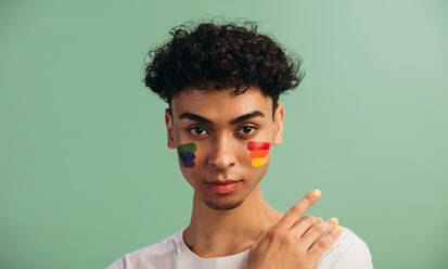Portrait of a young man with LGBT flag painted on his cheeks. Theme of equality and freedom of choice. - JLPSF05696