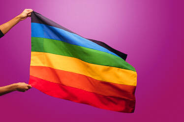 Cropped Schuss der Hände halten Homosexuell Stolz Flagge gegen lila Hintergrund. Regenbogenfarben lgbt Stolz Flagge. - JLPSF05704