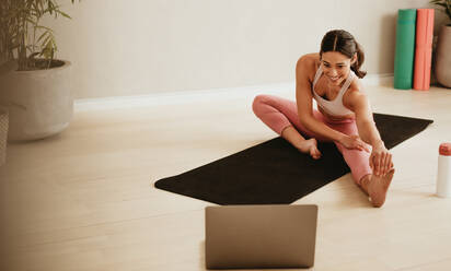 Weiblicher Fitnesstrainer unterrichtet Beindehnungsübungen online am Laptop. Frau trainiert vor ihrem Laptop im Fitnessstudio. - JLPSF05739