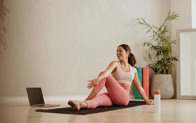 Active woman practicing yoga while E-learning through laptop at