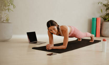 Frau lächelt beim Training im Fitnessstudio. Frau in Sportkleidung hält Plank-Position auf Übungsmatte zu Hause. - JLPSF05743