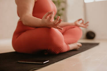 Frau sitzt auf Fitnessmatte mit gekreuzten Beinen und Händen auf den Knien in Yoga-Pose. Frau meditiert in Lotus-Pose im Fitnessstudio. - JLPSF05774