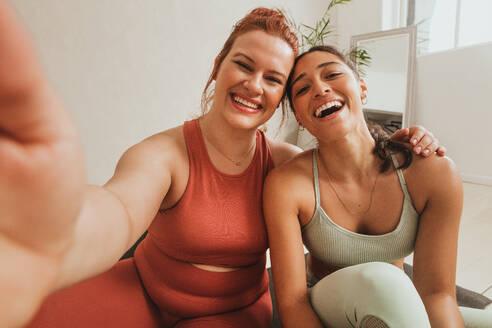 Smiling women taking self portrait at health club. Female friends in fitness studio taking selfie. - JLPSF05798