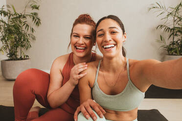 Fröhliche Freundinnen machen ein Selfie im Yoga-Studio. Frauen in Sportkleidung machen eine Pause vom Training und machen ein Selfie im Fitness-Studio. - JLPSF05799