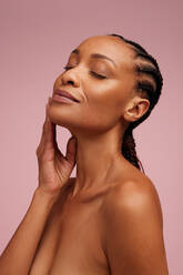African american female touching smooth and healthy skin of her face. Woman with beautiful skin pampering her face skin and eyes closed. - JLPSF05833