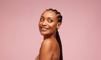 Attractive woman with clean and clear skin looking away. Female model having braided hairstyle standing against pink background. - JLPSF05842