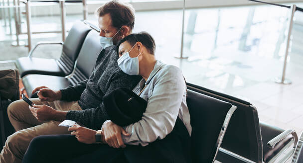 Ein Mann und eine Frau, die während der Pandemie im Flughafenterminal sitzen, tragen Gesichtsmasken und warten auf einen verspäteten Flug. - JLPSF05936