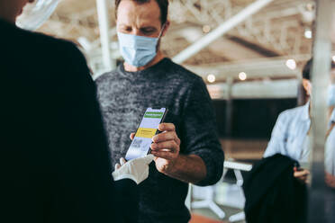 Ein Mann mit Gesichtsmaske zeigt dem Flughafenpersonal seinen Covid-19-Impfpass auf dem Handy. Ein Reisender am Flughafen-Check-in-Schalter zeigt dem Flugbegleiter seinen Impfpass. - JLPSF05942