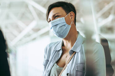 Reisende Frau mit Gesichtsmaske am Flughafen. Weiblicher Passagier während der Coronavirus-Pandemie am Flughafen. - JLPSF05945
