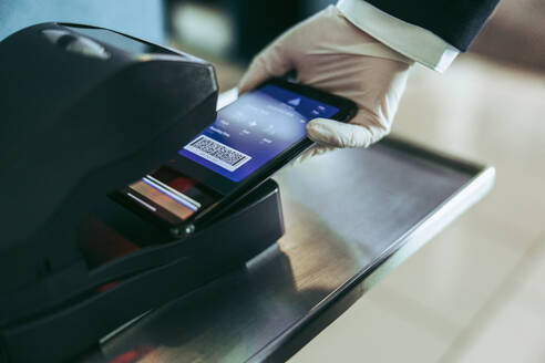 Scannen der Bordkarte auf dem Mobiltelefon am Flughafenschalter. Ausschnitt eines Flughafenmitarbeiters, der die Bordkarte mit der Hand am Gerät scannt. - JLPSF05954
