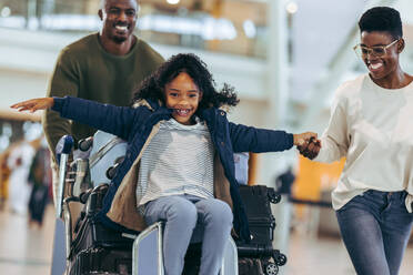 Man and woman going on a holiday with young girl sitting on luggage trolley at airport. African family having fun at airport terminal while going on holiday. - JLPSF05971