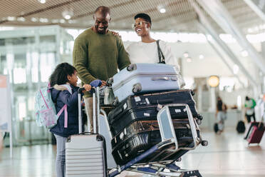 Familie steht am Flughafen-Terminal und wartet auf ihren Flug. Eltern mit Tochter am Flughafen mit ihrem Gepäck auf einem Trolley. - JLPSF05974