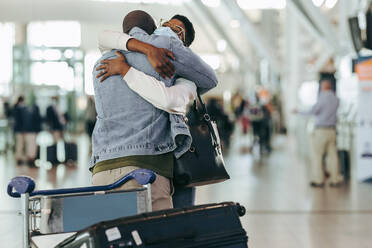 African couple met in airport after separation due to covid. Man and woman hugging each other at arrival gate at airport terminal. - JLPSF05980
