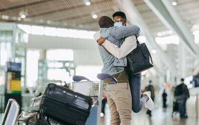 African man hugging and lifting woman at airport terminal. Couple meet after long separation at airport post pandemic lockdown. - JLPSF05983