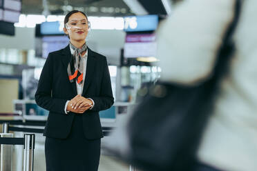 Flugbegleiter mit Gesichtsschutz auf dem Flughafen. Flughafenpersonal während der Pandemie, das Reisende willkommen heißt. - JLPSF05988