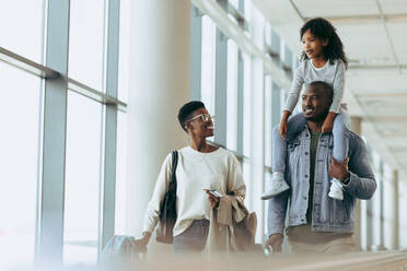 Girl on shoulder of father while walking with mother at airport. Happy family going on holiday. - JLPSF05999