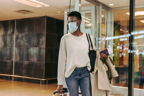 Afrikanische Frau mit Gesichtsmaske, die am Flughafen spazieren geht. Junge Frau, die während des Ausbruchs von Covid-19 reist. - JLPSF06001