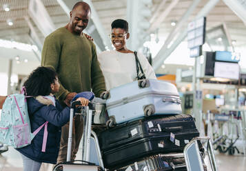 Glückliche Eltern und junge Tochter mit Gepäck am Flughafen stehend. Afrikanische dreiköpfige Familie am Flughafenterminal, die auf ihren Flug wartet. - JLPSF06012