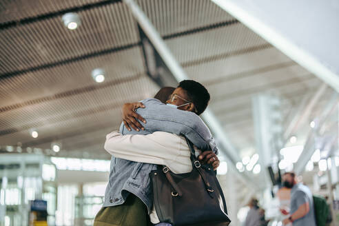 Ein Paar umarmt sich auf dem Flughafen während einer Pandemie. Ein Mann umarmt eine Frau, bevor er sich im Flughafenterminal von ihr verabschiedet. - JLPSF06015