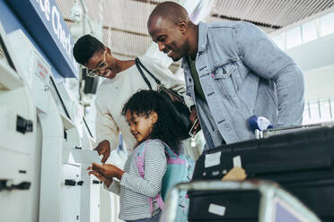 Familie am Self-Check-in-Automaten eines internationalen Flughafens. Kleines Mädchen mit Familie, das im Flughafenterminal die Bordkarte betrachtet. - JLPSF06023