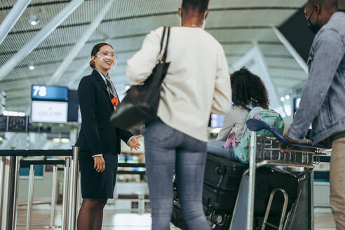 Flughafenpersonal während der Pandemie, das einer Familie von Reisenden am Flugsteig hilft. Bodenpersonal am Flughafen, das Touristen während der Pandemie mit Gesichtsmasken hilft. - JLPSF06028