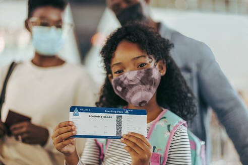 Ein Mädchen zeigt seine Bordkarte, während sie mit ihrer Familie am Flugsteig steht. Ein junges Mädchen und ihre Familie am Flughafen, die während einer Pandemie in den Urlaub fahren. - JLPSF06032