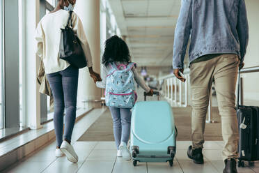 Rear view of a family with luggage walking in airport terminal. Family of three going on vacation. - JLPSF06036